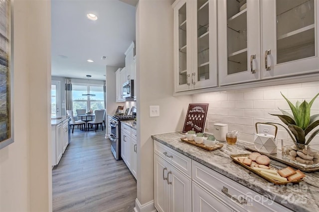 kitchen featuring light stone counters, light wood finished floors, stainless steel appliances, glass insert cabinets, and white cabinets