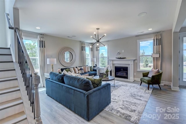 living area with a fireplace, light wood-style floors, a chandelier, baseboards, and stairs