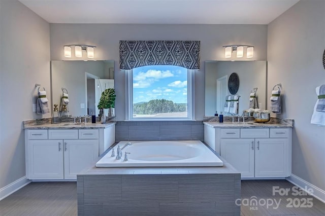 full bath featuring a sink, baseboards, two vanities, and a bath