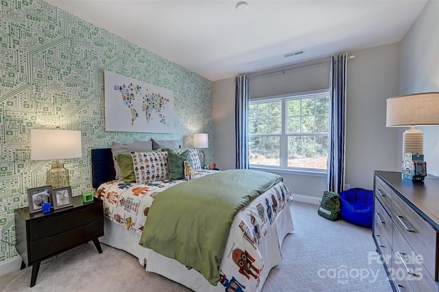 bedroom featuring light carpet, an accent wall, visible vents, baseboards, and wallpapered walls