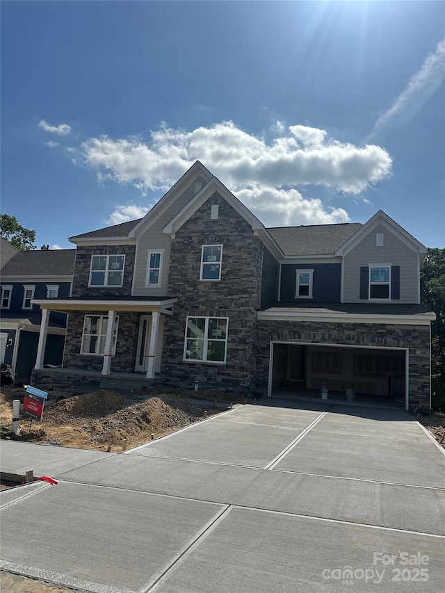 view of front facade with a porch, driveway, stone siding, and a garage