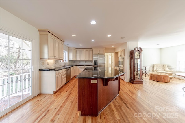 kitchen featuring appliances with stainless steel finishes, a kitchen bar, backsplash, light wood-type flooring, and a center island with sink