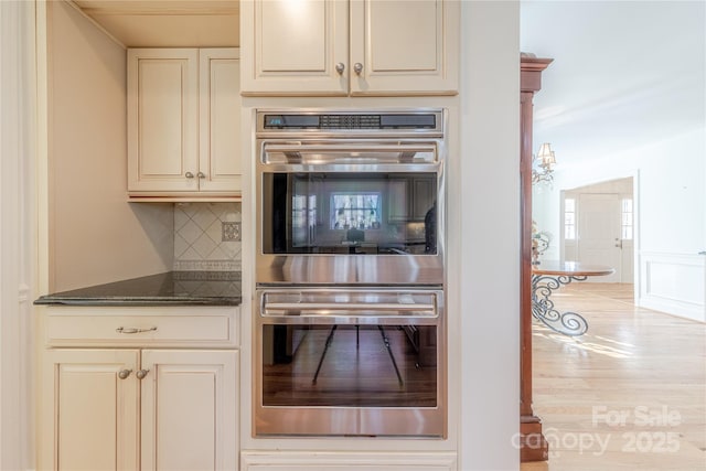 kitchen featuring dark stone countertops, double oven, backsplash, and cream cabinetry