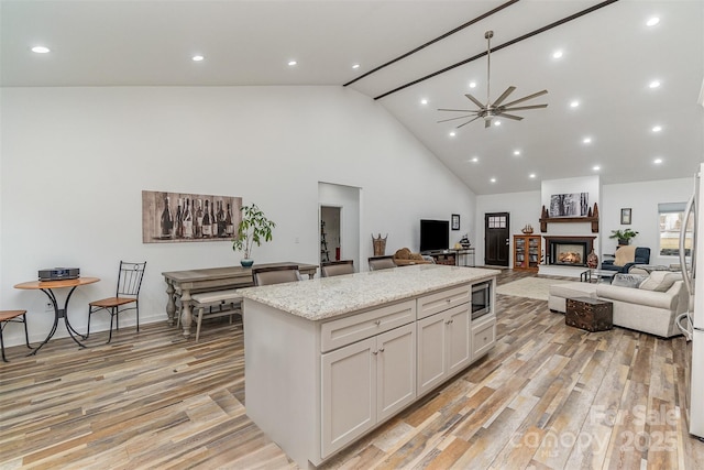 kitchen with light wood-style flooring, open floor plan, a center island, white cabinetry, and a lit fireplace