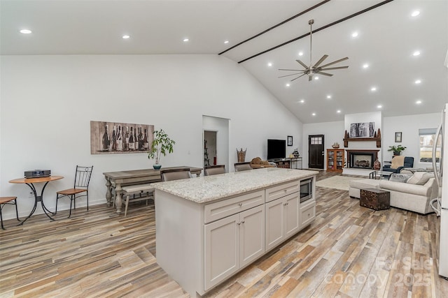 kitchen featuring a kitchen island, a fireplace with raised hearth, white cabinets, light wood-style floors, and open floor plan