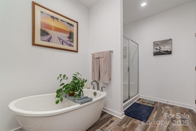 bathroom featuring wood finished floors, baseboards, recessed lighting, a stall shower, and a freestanding bath