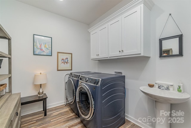 laundry area with washer and clothes dryer, a sink, cabinet space, light wood-style floors, and baseboards