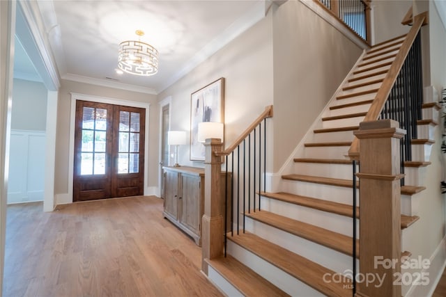 foyer entrance with light wood-type flooring, a chandelier, crown molding, and french doors