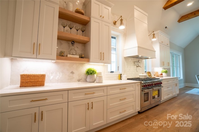 kitchen with white cabinetry, double oven range, backsplash, light wood-type flooring, and custom range hood