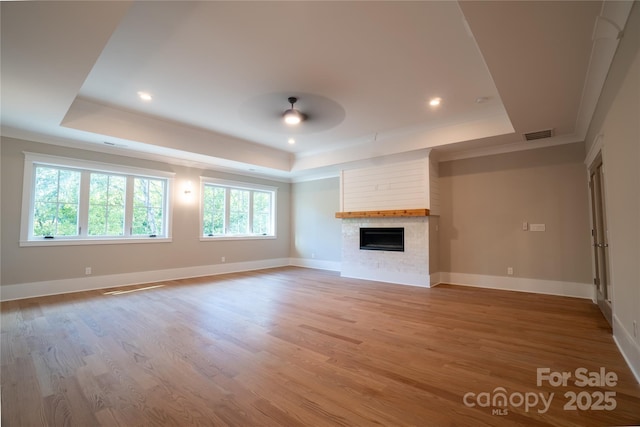 unfurnished living room featuring a wealth of natural light, a large fireplace, wood-type flooring, and a raised ceiling