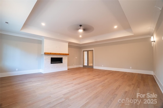 unfurnished living room with a raised ceiling, ceiling fan, a large fireplace, and crown molding