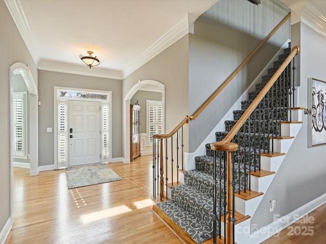 foyer entrance featuring baseboards, ornamental molding, arched walkways, and wood finished floors