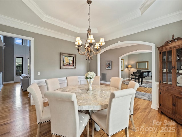 dining room with light wood-type flooring, visible vents, a raised ceiling, and arched walkways