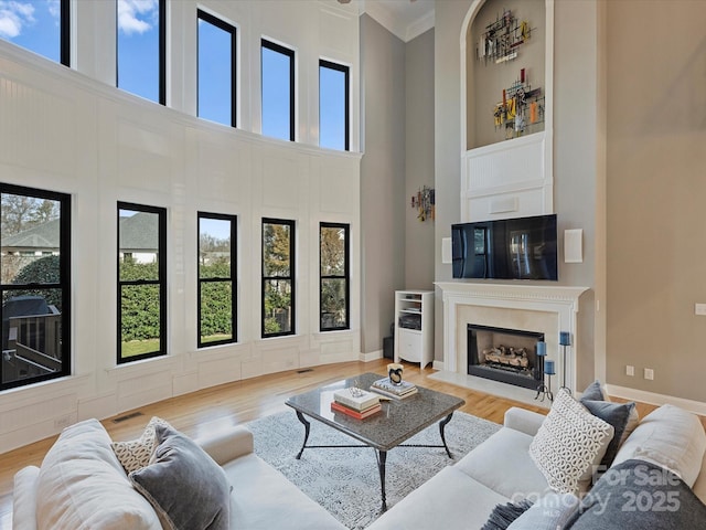 living room with light wood finished floors, a fireplace with flush hearth, a high ceiling, and crown molding