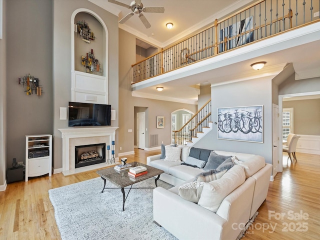 living room with a towering ceiling, light wood-style flooring, ornamental molding, stairs, and a fireplace