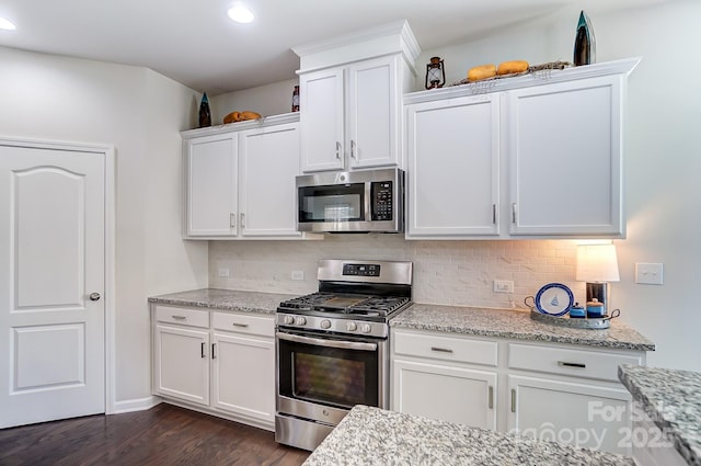 kitchen with light stone countertops, white cabinetry, appliances with stainless steel finishes, and dark hardwood / wood-style flooring