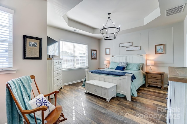 bedroom featuring an inviting chandelier, dark hardwood / wood-style flooring, and a tray ceiling