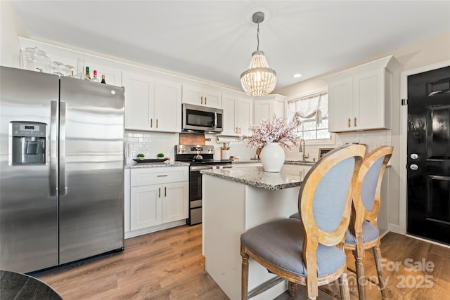 kitchen with white cabinetry, appliances with stainless steel finishes, decorative light fixtures, and light stone countertops