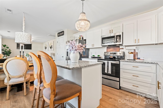 kitchen with appliances with stainless steel finishes, a kitchen island, white cabinetry, hanging light fixtures, and light stone counters