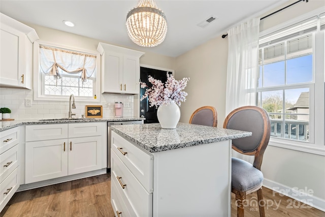 kitchen with sink, white cabinetry, a kitchen bar, decorative light fixtures, and light wood-type flooring