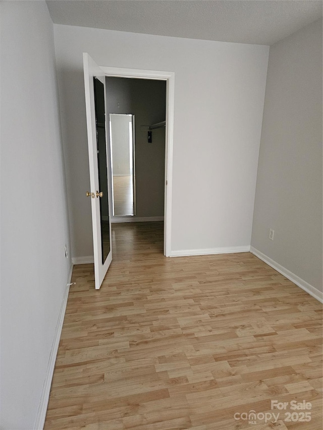 unfurnished room with a textured ceiling, light wood-style flooring, and baseboards