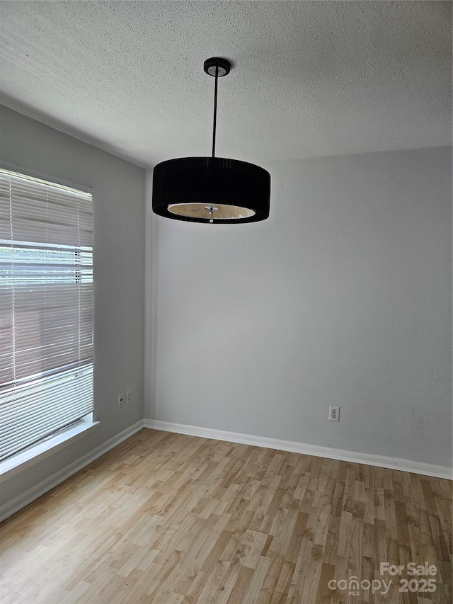 empty room with a textured ceiling, baseboards, and wood finished floors