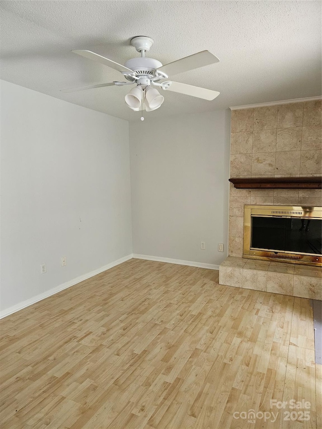 unfurnished living room with baseboards, a tile fireplace, ceiling fan, a textured ceiling, and light wood-style floors