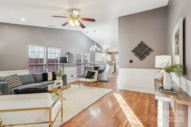 living room with light hardwood / wood-style floors, a textured ceiling, lofted ceiling, and ceiling fan with notable chandelier