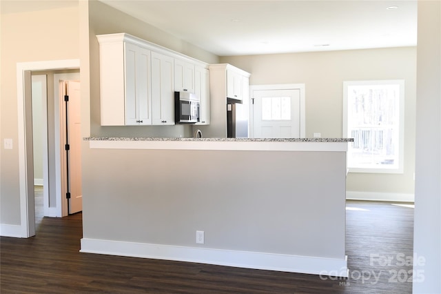 kitchen with dark wood-style flooring, appliances with stainless steel finishes, white cabinets, a peninsula, and baseboards