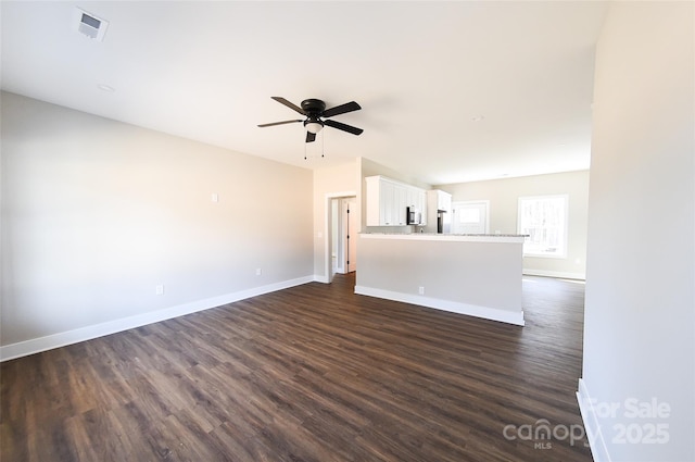 unfurnished living room featuring dark wood-type flooring, visible vents, ceiling fan, and baseboards