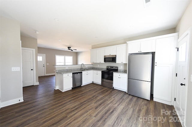 kitchen featuring appliances with stainless steel finishes, dark wood-type flooring, a peninsula, white cabinetry, and a sink