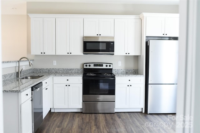 kitchen featuring stainless steel appliances, dark wood-type flooring, a sink, white cabinetry, and light stone countertops