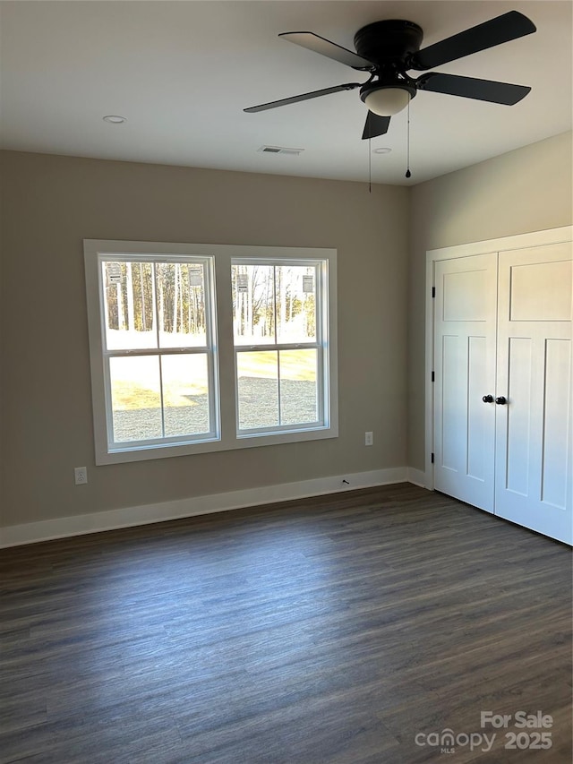 unfurnished bedroom featuring dark wood-type flooring, a ceiling fan, visible vents, baseboards, and a closet