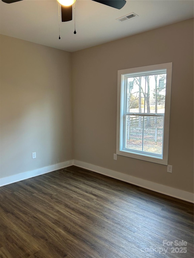 empty room with baseboards, ceiling fan, visible vents, and dark wood-type flooring