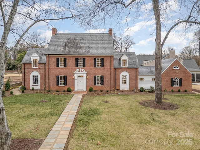 view of front of house featuring a high end roof, brick siding, a chimney, and a front lawn