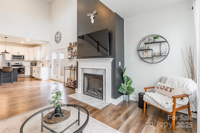 living room featuring light hardwood / wood-style floors, sink, a high ceiling, and a premium fireplace