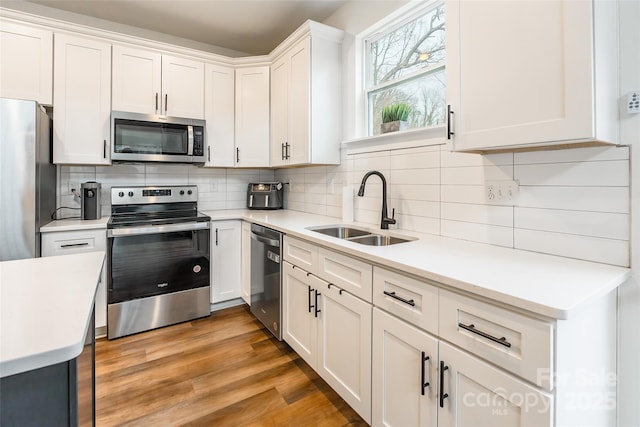 kitchen featuring white cabinetry, light hardwood / wood-style floors, appliances with stainless steel finishes, tasteful backsplash, and sink