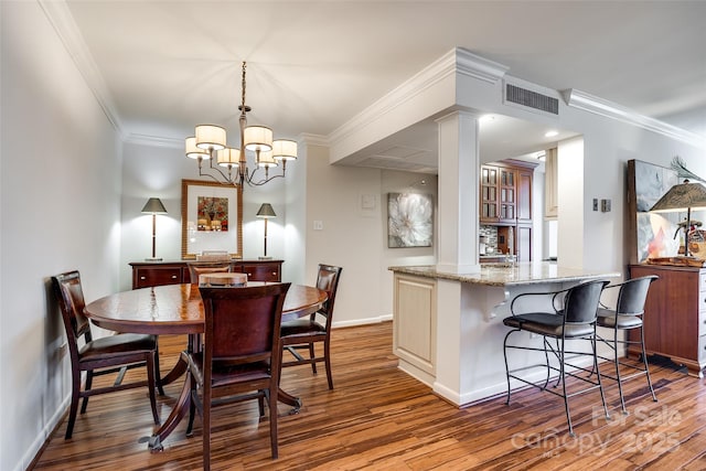 dining area featuring decorative columns, crown molding, dark hardwood / wood-style floors, and a notable chandelier