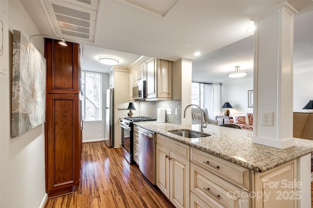 kitchen with sink, wood-type flooring, stainless steel appliances, light stone countertops, and cream cabinetry