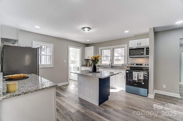 kitchen featuring light stone counters, white cabinetry, appliances with stainless steel finishes, and a center island