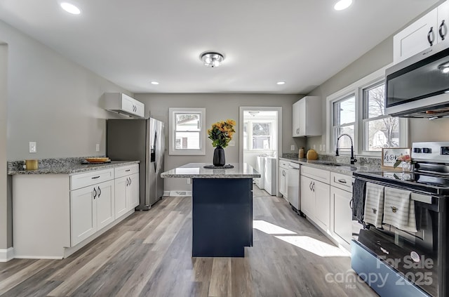 kitchen featuring appliances with stainless steel finishes, sink, light stone countertops, white cabinets, and a center island