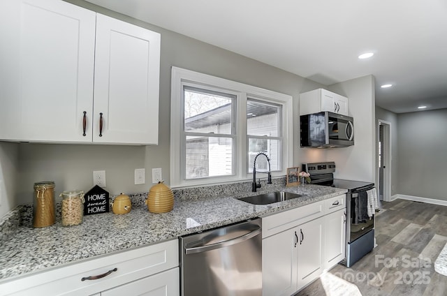 kitchen with sink, white cabinetry, light wood-type flooring, light stone countertops, and stainless steel appliances