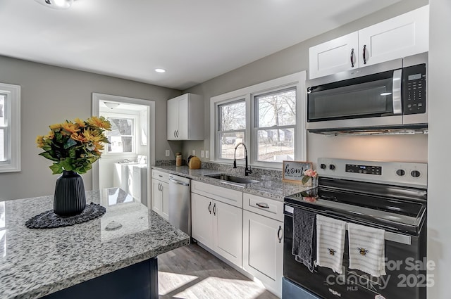 kitchen featuring washing machine and clothes dryer, stainless steel appliances, white cabinets, light stone counters, and sink