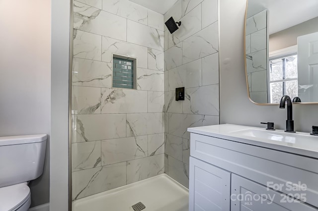 bathroom with toilet, tiled shower, and vanity