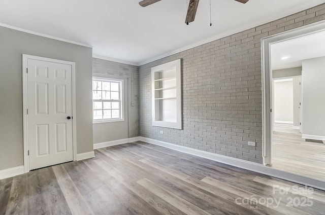 empty room with brick wall, built in shelves, light hardwood / wood-style floors, ornamental molding, and ceiling fan