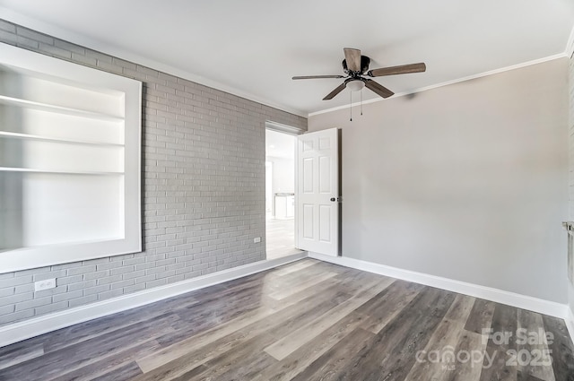 empty room with ceiling fan, wood-type flooring, brick wall, and crown molding