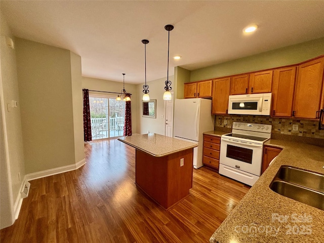 kitchen with pendant lighting, tasteful backsplash, light stone countertops, white appliances, and a center island