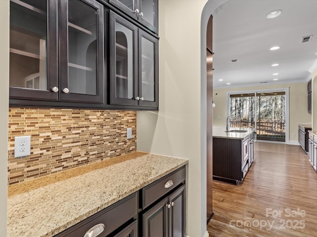 kitchen with sink, crown molding, light hardwood / wood-style flooring, light stone counters, and tasteful backsplash