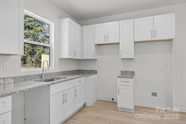 kitchen featuring light stone counters, white cabinetry, a sink, and light wood finished floors