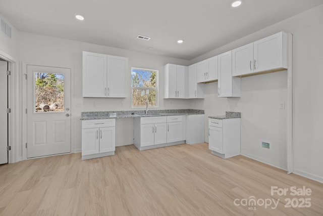 kitchen with light wood-style flooring, a sink, visible vents, and white cabinets